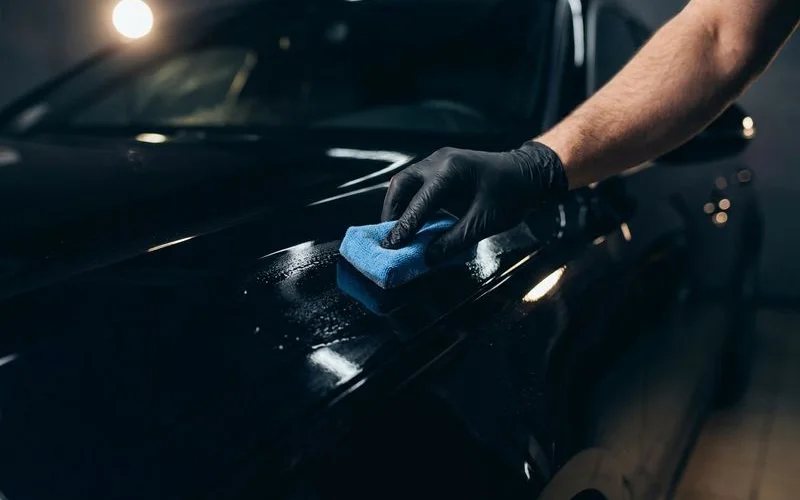 Professional ceramic coating being carefully applied to a vehicle's paint surface using a foam applicator pad