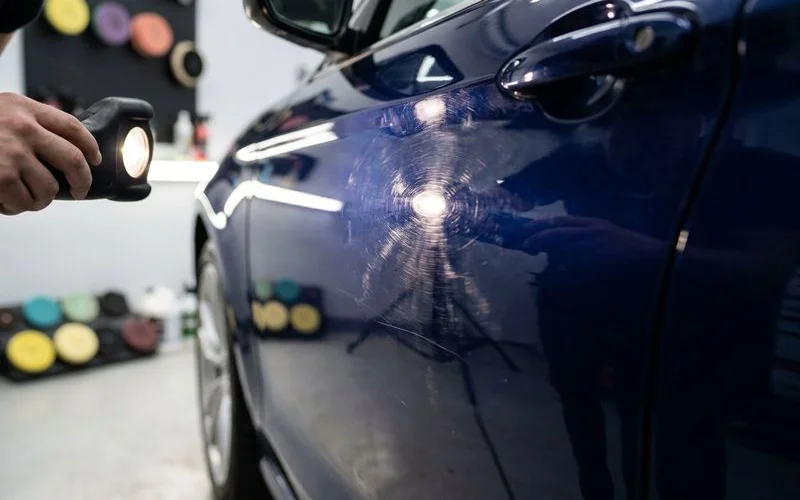 Close up view of swirl marks on black vehicle hood visible under bright LED inspection light source